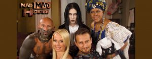 A heavily tattooed man, a pretty blonde, a man who looks like a movie vampire character, a handsome man, and a lovely lady with perhaps African inspired headwear.